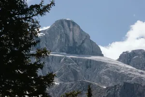 A stunning view of a rocky mountain peak in Austria framed by pine trees against a blue sky. jigsaw puzzle