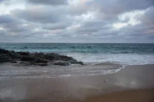 Peaceful beach scene with waves crashing on rocks under a cloudy sky. jigsaw puzzle