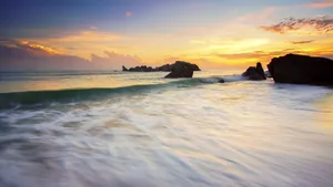 Stunning sunset over a rocky beach with waves and colorful sky, perfect for summer travel inspiration. jigsaw puzzle