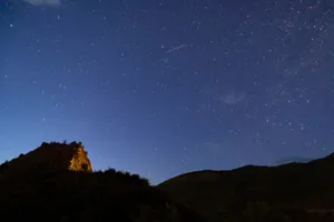 A breathtaking view of a clear starry sky with a meteor streak above a silhouetted mountain landscape at night. jigsaw puzzle