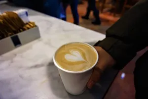 A hand holds a cup of coffee with elegant latte art on a marble countertop in a cozy cafe. jigsaw puzzle