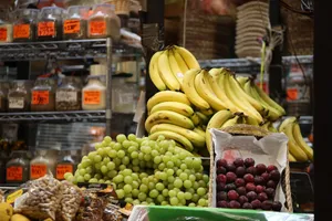 A vibrant assortment of bananas, grapes, and plums at a bustling market stand. jigsaw puzzle