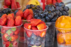 Vibrant strawberries, grapes, and persimmons displayed in plastic cups at a market. jigsaw puzzle