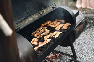 Close-up of a barbecue grill outdoors with various meat strips cooking, exuding rich smoke. jigsaw puzzle