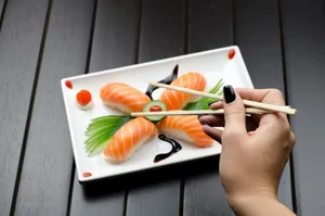 Close-up of a sushi plate with salmon nigiri and decorative garnish, held with chopsticks. jigsaw puzzle