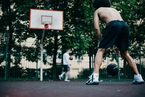 Two athletes playing basketball shirtless on an outdoor court with trees surrounding. jigsaw puzzle