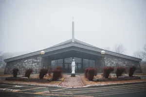 Facade of contemporary catholic church located among leafless trees in rainy weather in daytime jigsaw puzzle