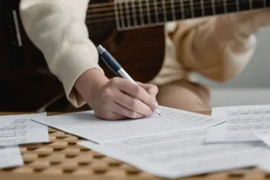 Person writing music on sheet paper with an acoustic guitar in a cozy home setting. jigsaw puzzle