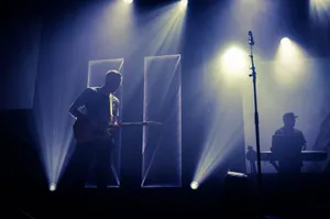 Anonymous male musician performing melody with guitar on stage near microphone and DJ in dark club with spotlights jigsaw puzzle