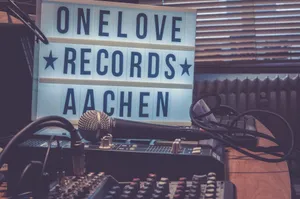 A warm-toned studio featuring a microphone, audio mixer, and lightbox signage reading 'One Love Records Aachen'. jigsaw puzzle