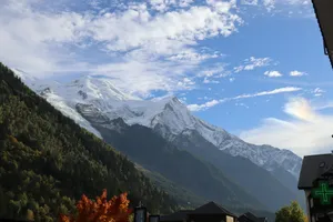 Snow-capped mountains rise above a green forest under blue sky. jigsaw puzzle