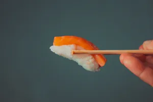 a hand holding a piece of sushi with chopsticks jigsaw puzzle