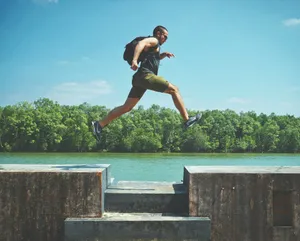 man leaping on concrete surface near body of water and forest at the distance during day jigsaw puzzle