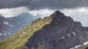 Dramatic mountain landscape with rocky peaks, green slopes, and swirling clouds. jigsaw puzzle