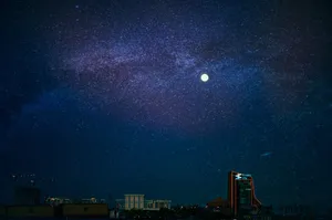 Vibrant city skyline beneath a starry night sky with a prominent full moon. jigsaw puzzle