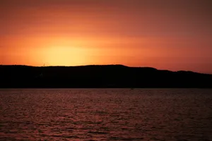 Peaceful ocean scene at sunset with silhouetted hills and vibrant sky. jigsaw puzzle