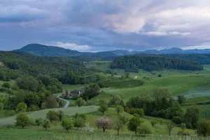 Lush green countryside with rolling hills under a dramatic cloudy sky during summer. jigsaw puzzle