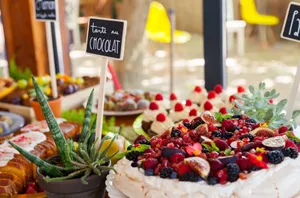 A colorful fruit cake surrounded by an array of desserts on an outdoor table setting. jigsaw puzzle