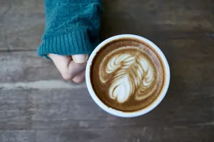 Cozy shot of a person holding a creatively styled cup of latte on a wooden table. jigsaw puzzle
