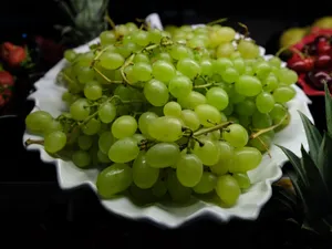 A vibrant close-up of fresh green grapes on a white plate, perfect for healthy food themes. jigsaw puzzle
