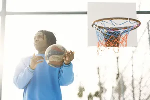 Young man in blue sweatshirt holding a basketball on an outdoor court. jigsaw puzzle