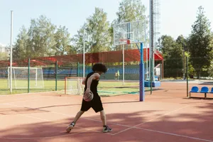 A young man dribbles a basketball on an outdoor court with surrounding greenery. jigsaw puzzle