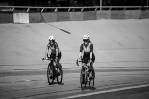 Two women cyclists riding on a velodrome track, captured in a black and white photo. jigsaw puzzle