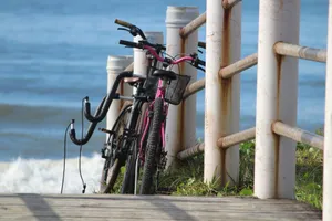 Two bicycles rest against a fence by the ocean in Guaratuba, Brazil, offering a serene coastal scene. jigsaw puzzle