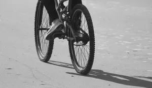 Monochrome image of a cyclist riding a bicycle on a sandy beach, highlighting motion and texture. jigsaw puzzle
