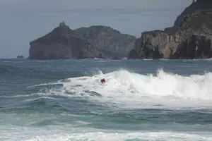 A surfer catching waves with a rocky coastline in the background, showcasing the surf lifestyle. jigsaw puzzle