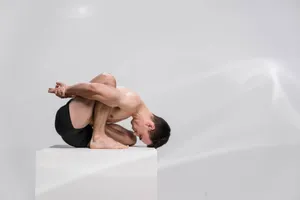 A highly flexible man demonstrates an advanced contortion pose on a white platform in a minimalist studio. jigsaw puzzle