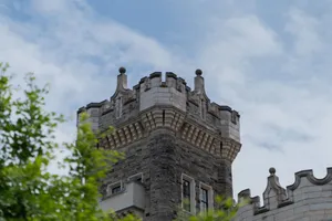 A majestic stone castle tower reaching towards a blue sky, surrounded by greenery. jigsaw puzzle