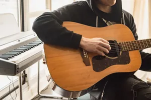 A musician playing an acoustic guitar next to a digital keyboard in a cozy indoor setting. jigsaw puzzle