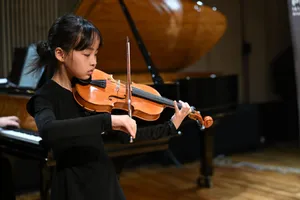 A young girl passionately playing the violin on stage, with a grand piano in the background. jigsaw puzzle