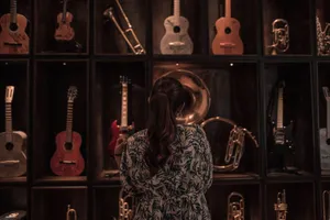 A woman observes a diverse collection of musical instruments on display, including guitars and trumpets, in a dimly lit room. jigsaw puzzle