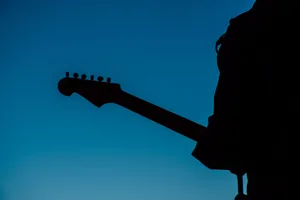 Silhouette of an adult playing an electric guitar against a clear blue sky, creating a dramatic and artistic scene. jigsaw puzzle