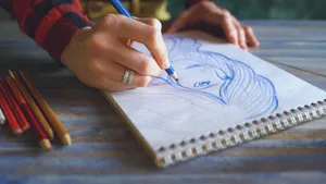Close-up of a hand sketching a portrait on a spiral sketchpad with colored pencils on a table. jigsaw puzzle