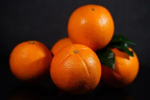 A stack of fresh oranges with green leaves, showcasing their vibrant color on a dark background. jigsaw puzzle