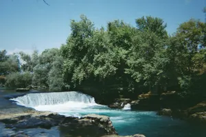 A picturesque waterfall cascading through a lush forest under a clear blue sky. jigsaw puzzle