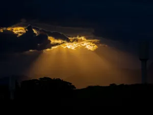 A captivating sunset with dramatic sun rays shining through dark clouds over a mountainous landscape. jigsaw puzzle
