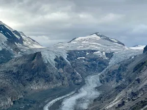 A stunning aerial view of a frozen glacier amidst a snow-capped mountain range under a cloudy sky. jigsaw puzzle