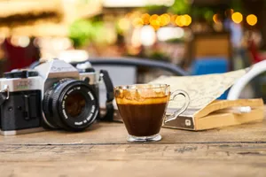 A warm espresso cup and vintage camera on a wooden table in an outdoor café setting. jigsaw puzzle