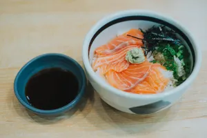 A vibrant salmon sashimi bowl garnished with wasabi, scallions, and seaweed, served with soy sauce. jigsaw puzzle