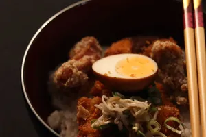 Close-up of Japanese karaage rice bowl topped with sliced egg and scallions, accompanied by chopsticks. jigsaw puzzle