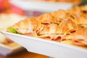 Close-up view of fresh croissant sandwiches with ham, cheese, and lettuce on a white plate. jigsaw puzzle