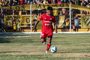 A soccer player in red uniform dribbling during a daytime match with spectators. jigsaw puzzle