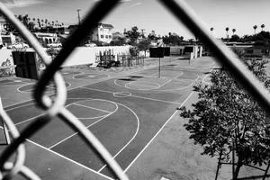 Black and white image of an outdoor basketball court viewed through a chain-link fence. jigsaw puzzle