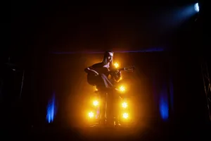 A musician playing an acoustic guitar on stage, illuminated by dramatic yellow and blue lights. jigsaw puzzle