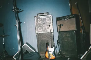 A vintage electric bass guitar stands against music amplifiers in a studio setting. jigsaw puzzle