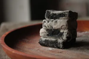 Close-up of ash-covered charcoal blocks stacked on a wooden plate, indoor setting. jigsaw puzzle